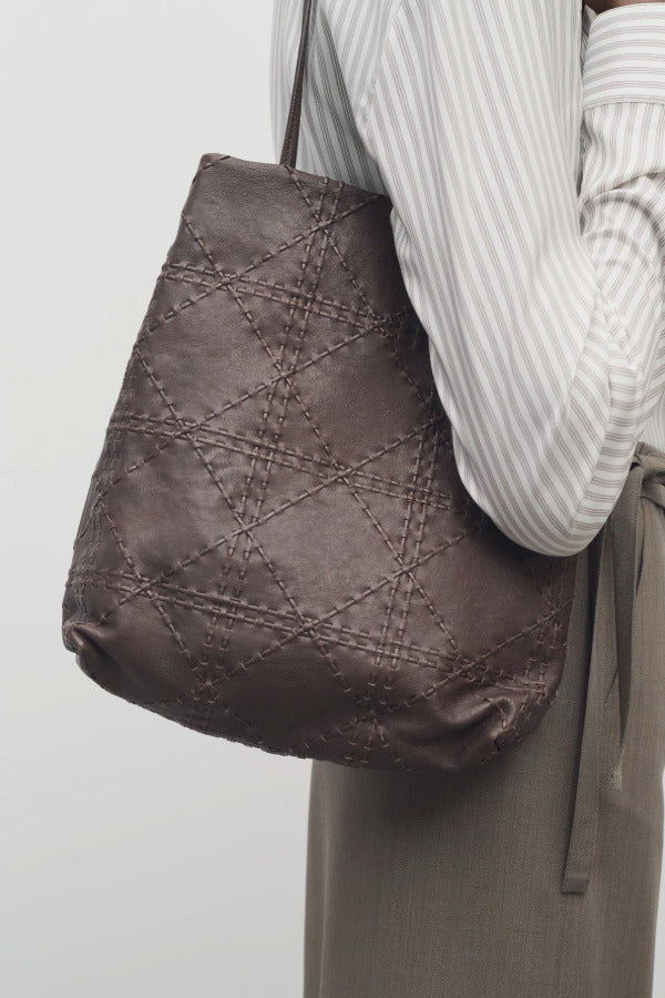 Front view of brown lilou woven tote on model wearing light stripe shirt and khaki pants against a white background.
