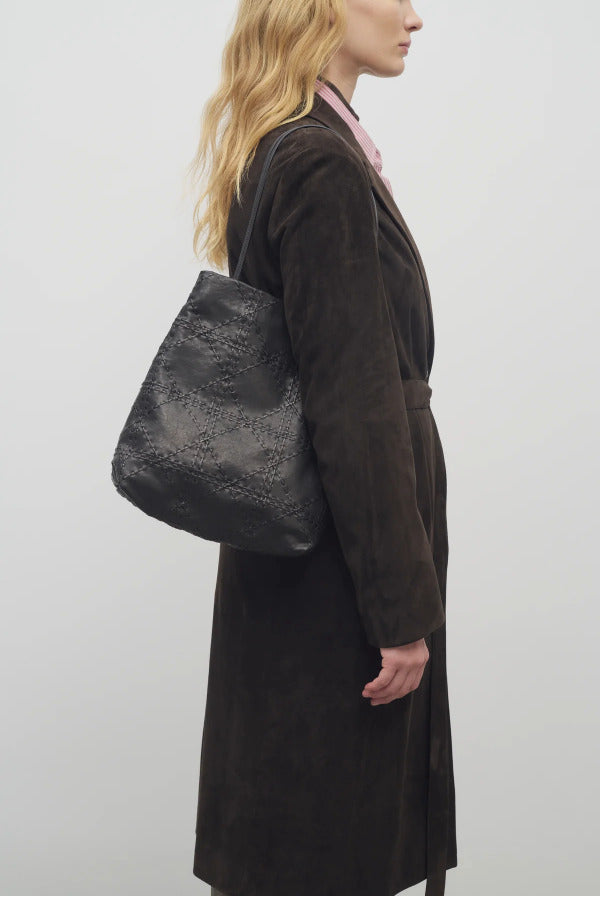 Front view of black lilou woven tote on model wearing brown overcoat against a white backround.