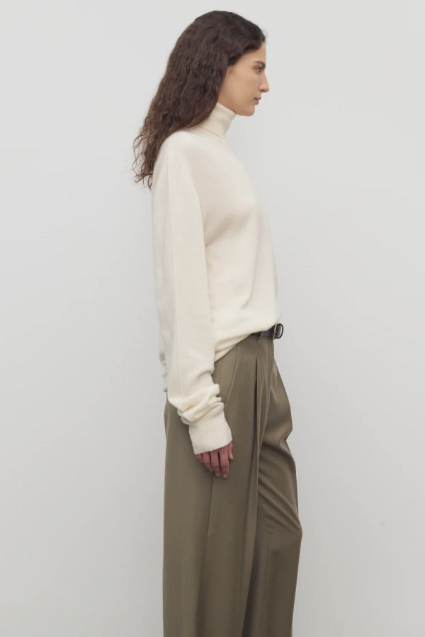 Side view of ivory lizzy top on model wearing khaki trousers and a brown belt, against a white background.