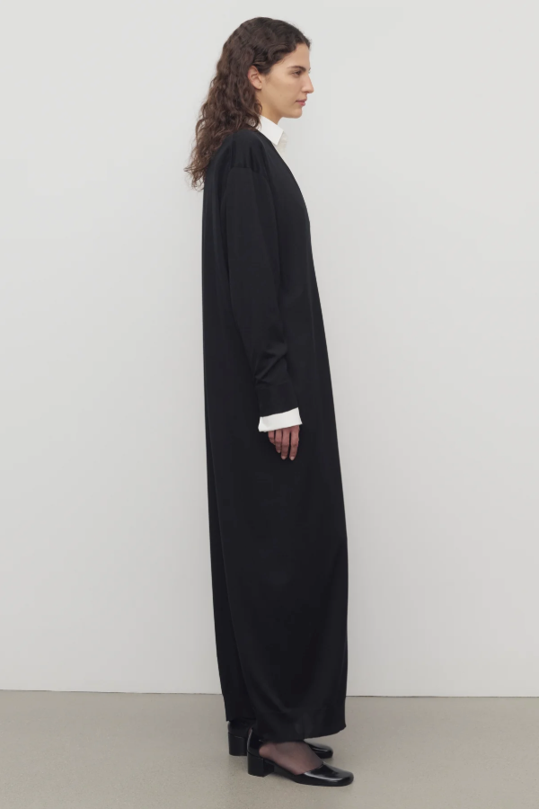 Side view of black luza dress on model wearing white collar shirt and black wedges, against a white background.