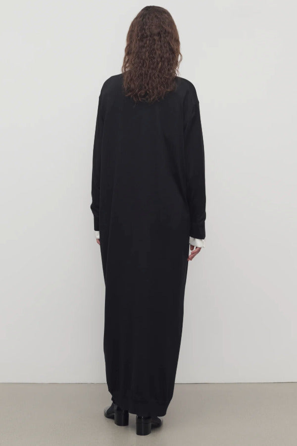 Back view of black luza dress on model wearing white collar shirt and black wedges, against a white background.