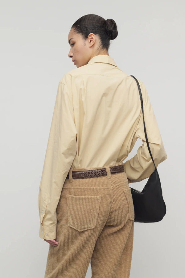 Back view of sand margan shirt on model wearing orange corduroys, brown belt and brown shoulder bag , against a white background.