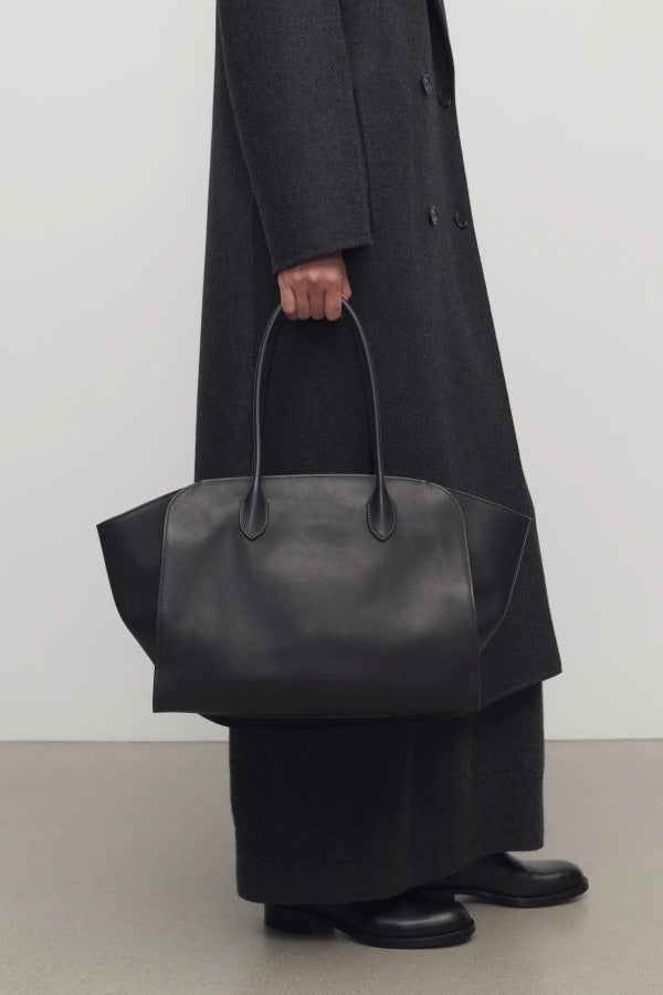 Front view of black marlo 14 bag on model wearing long black coat and boots, against a white background.