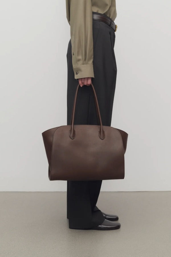 Front view of deep brown marlo 14 bag on model wearing black pants and green shirt, against a white background.