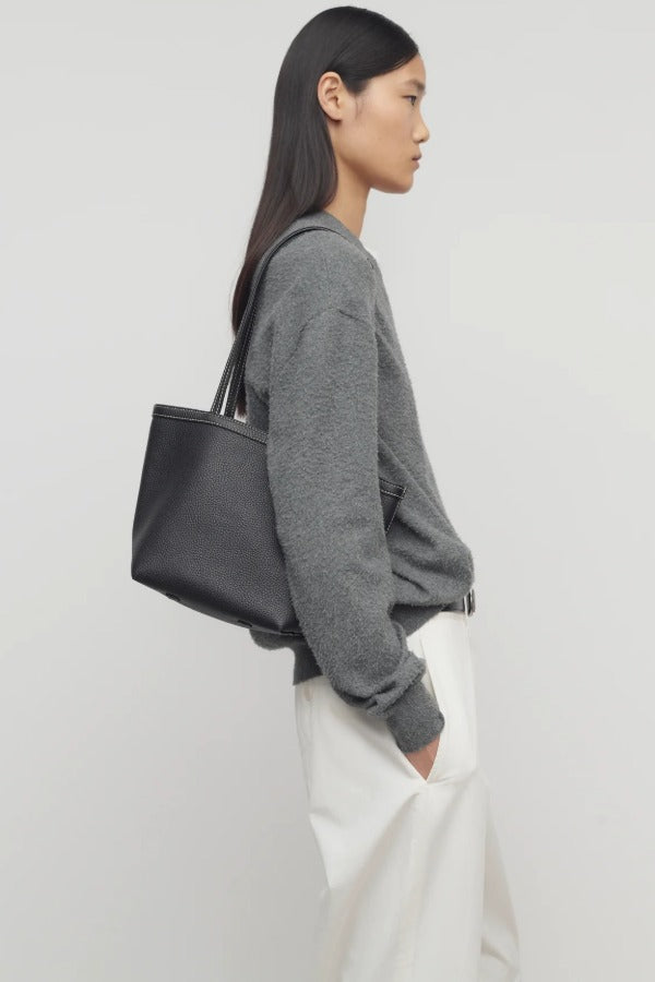 Front view of black medium park tote on model wearing white pants and a grey sweater, against a white background.