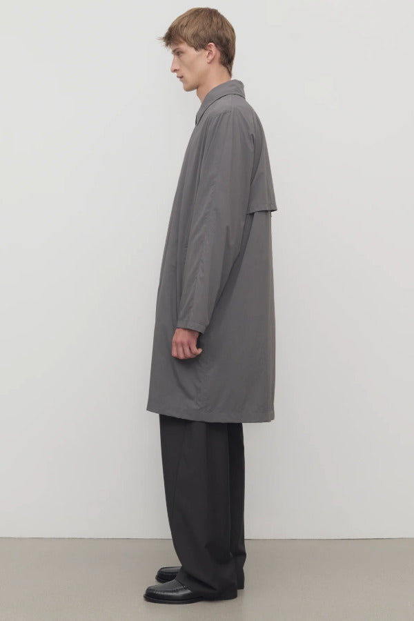 Side view of grey cobalt men's hesper coat on model wearing black pants and boots, against a white background.
