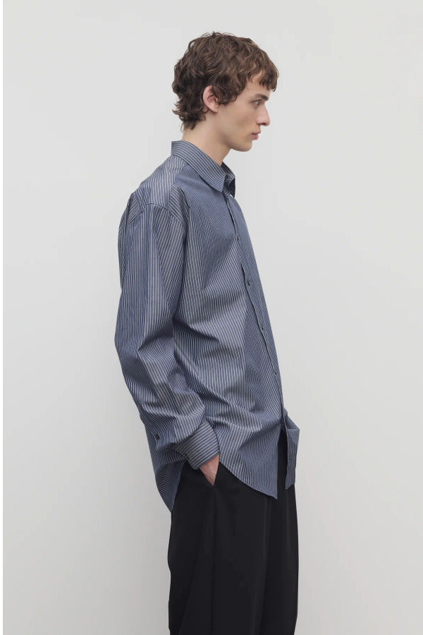 Side view of blue/white men's miller stripe shirt on model wearing black trousers, against a white background.