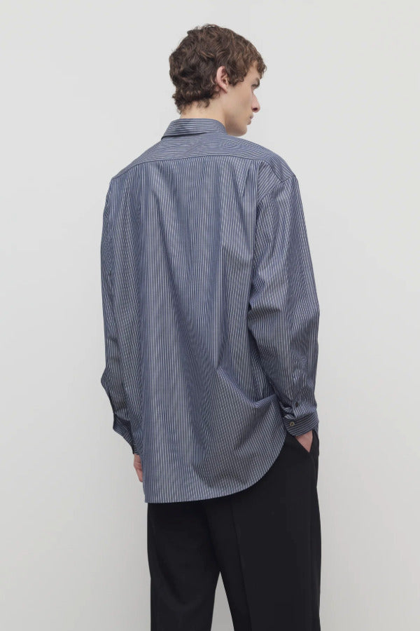Back view of blue/white men's miller stripe shirt on model wearing black trousers, against a white background.