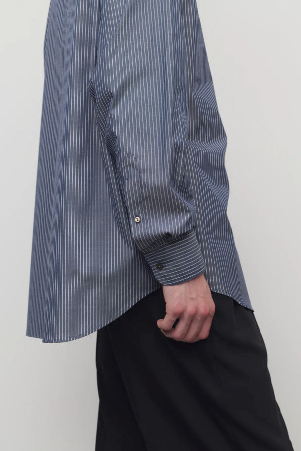 Closeup side view of blue/white men's miller stripe shirt on model wearing black trousers, against a white background.