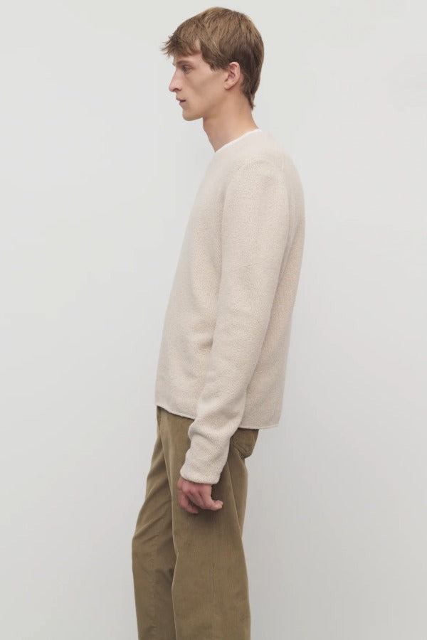 Side view of ecru nikola sweater on model wearing khakis against a white background.