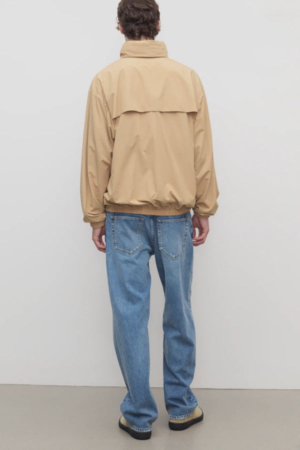 Back view of medium blue ross jean on model wearing sand windbreaker and sneakers, against a white background.