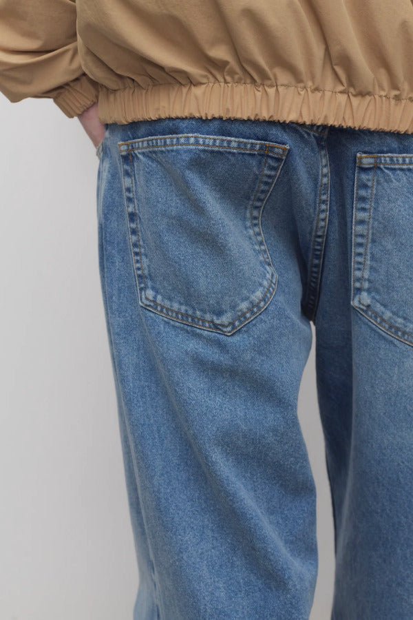 Back closeup view of medium blue ross jean on model wearing sand windbreaker, against a white background.