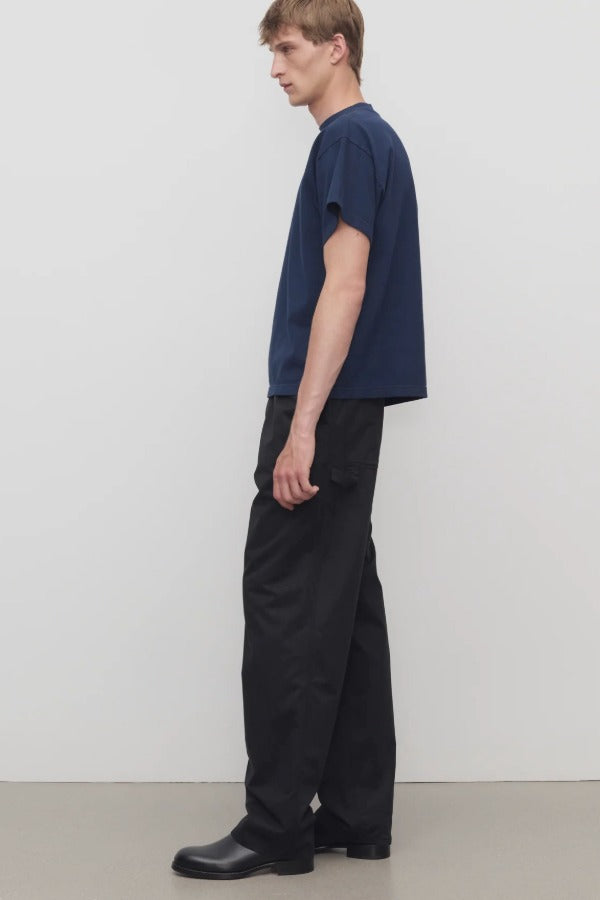 Side view of black sankuro pant on model wearing navy t-shirt and boots, against a white background.