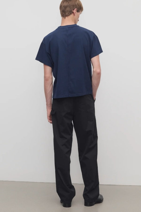 Back view of black sankuro pant on model wearing navy t-shirt and boots, against a white background.