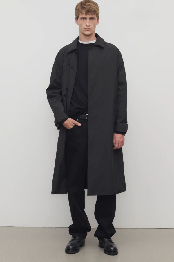 Front view of black tarian coat on model wearing black pants, shirt and boots, against a white background.