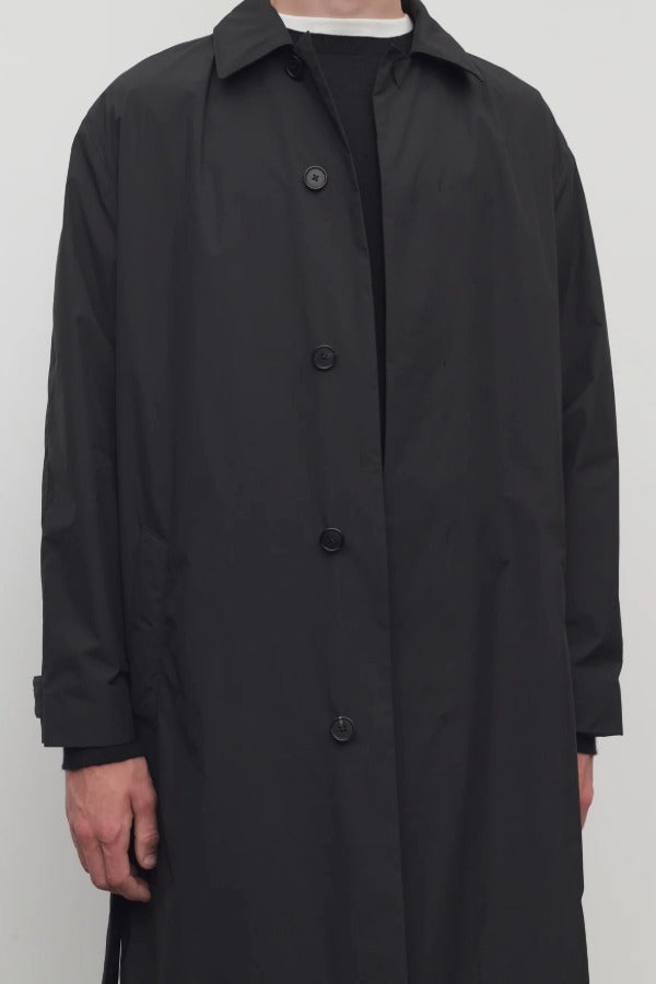 Front closeup of black tarian coat on model wearing black pants and shirt, against a white background.