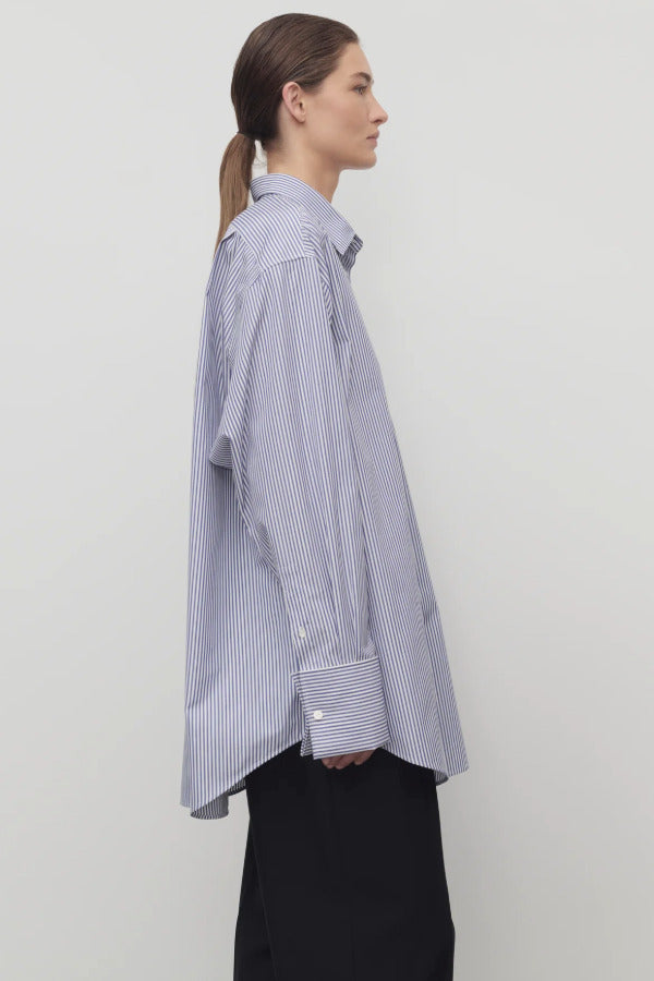 Side view of white and blue Ment shirt on a model wearing black trousers, against a white background.