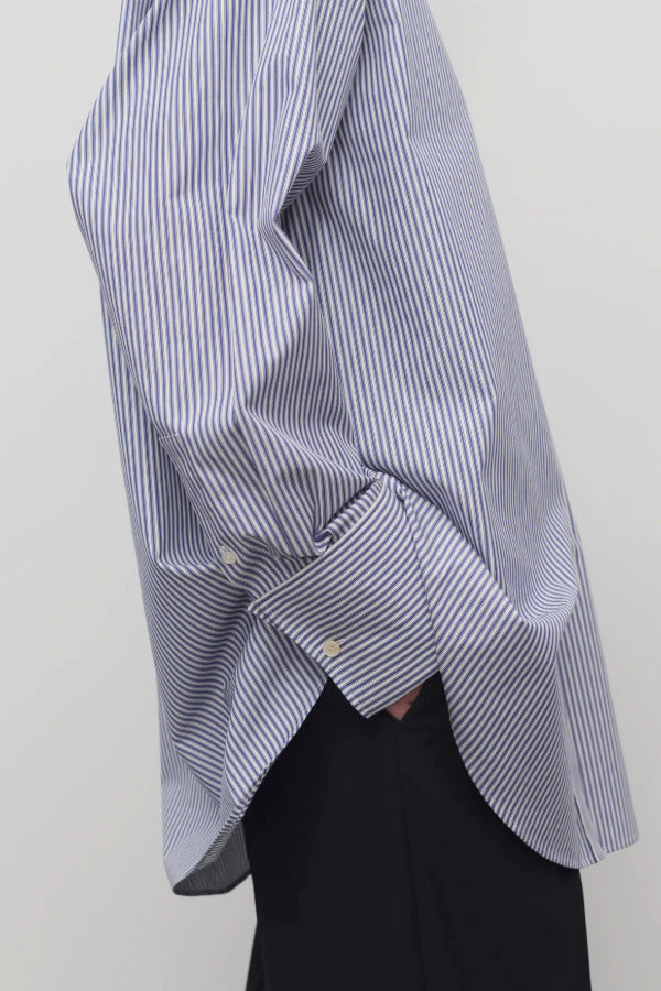 Side closeup view of white and blue shirt on model wearing black trousers, against a white background.