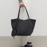 Front view of black park tote three canvas on model wearing white pants and grey sweater with mules, against a white background.