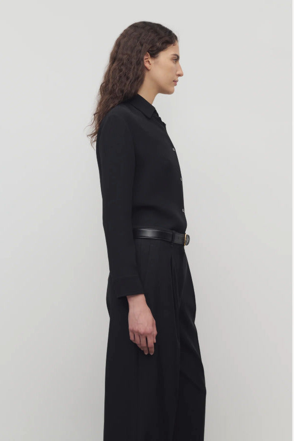 Side view of black petra shirt on model wearing black trousers, against a white background.