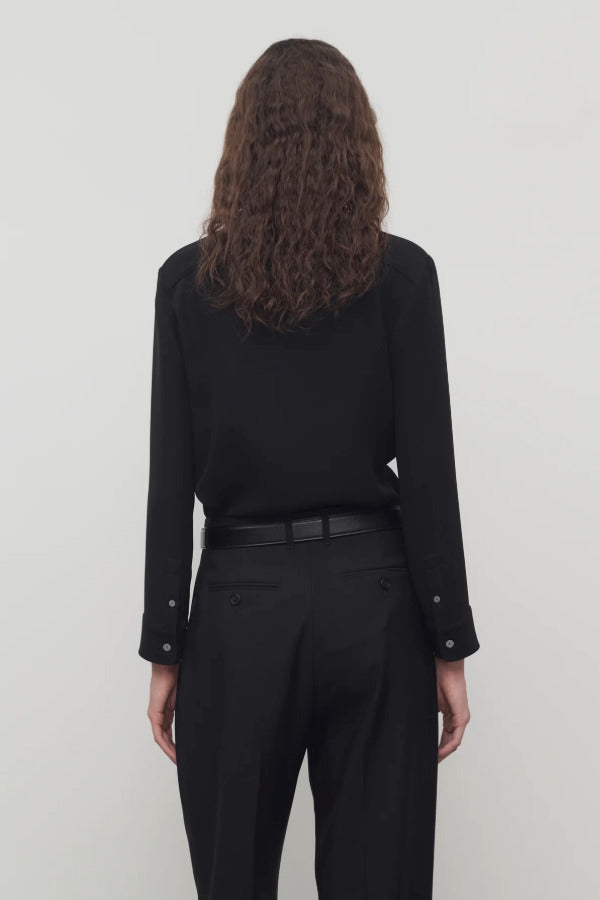 Back view of black petra shirt on model wearing black trousers, against a white background.