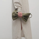 Front view of sage Nan Shoulder Bag on model scrunching the bag to show its flexibility against a white background.