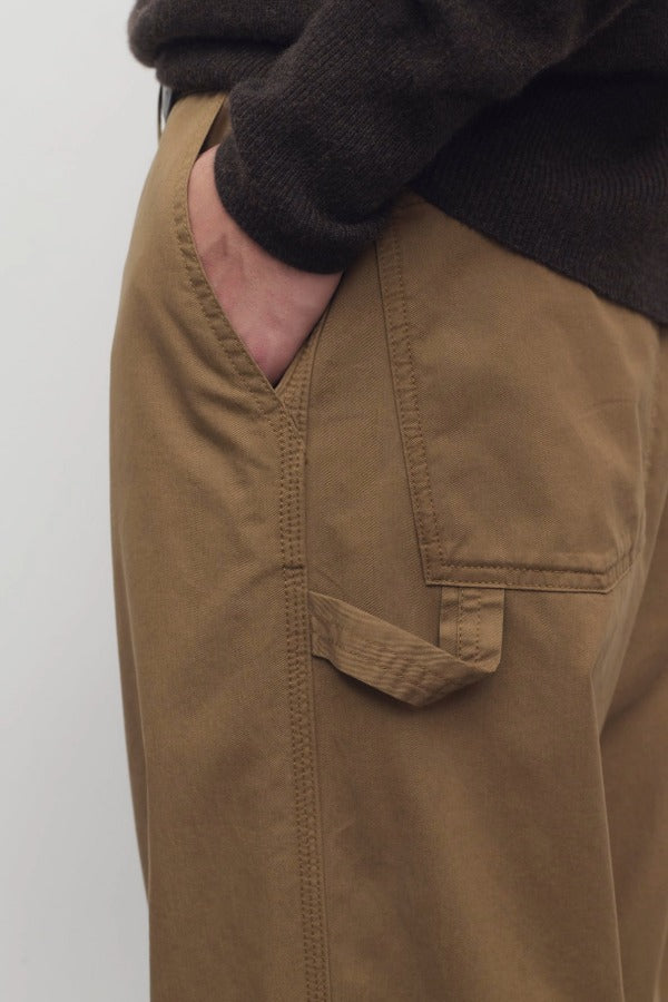 Side closeup view of dark sand sharka pant on model wearing black top, against a white background.
