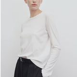 Front slanted view of white sherman t-shirt on model wearing black trousers, against a white background.