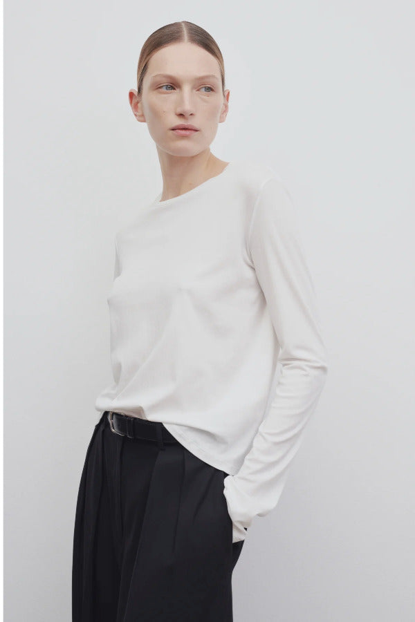 Front slanted view of white sherman t-shirt on model wearing black trousers, against a white background.