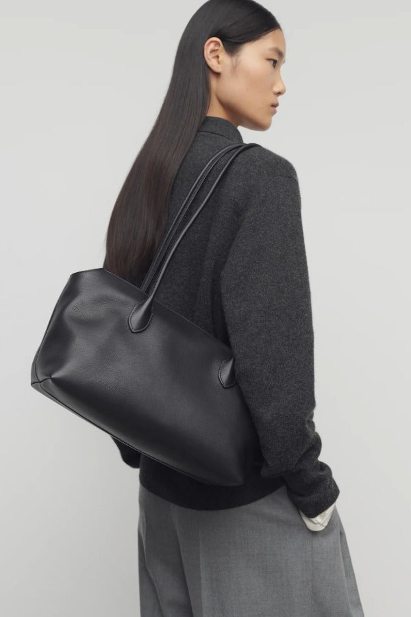 Front view of black terrasse bag on model wearing grey pants and charcoal sweater, against a white background.