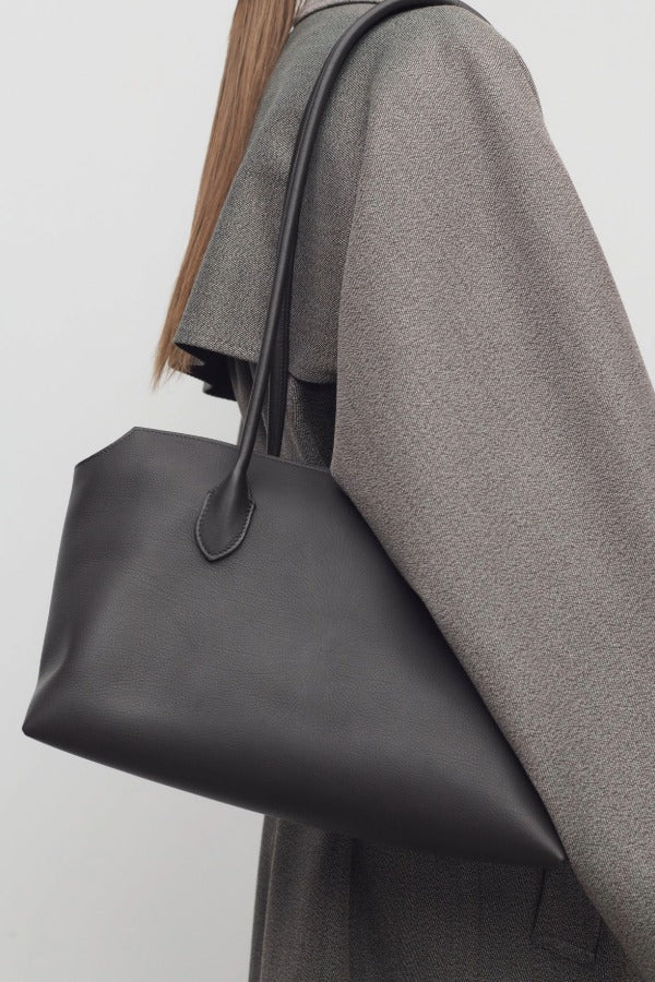 Front view of dark brown terrasse bag on model wearing grey coat, against a white background.