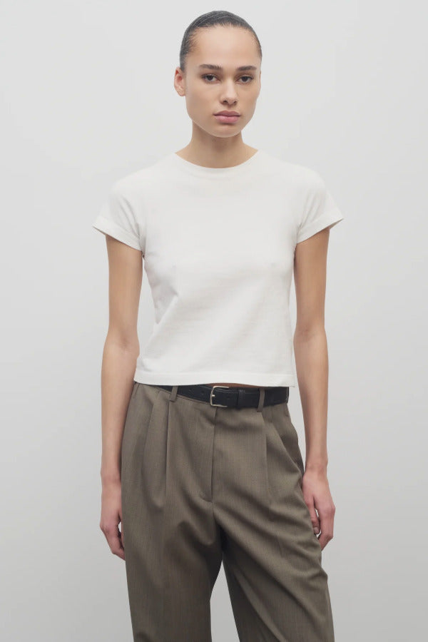 Front view of white tori top on model wearing khaki trousers and black belt, against white background.