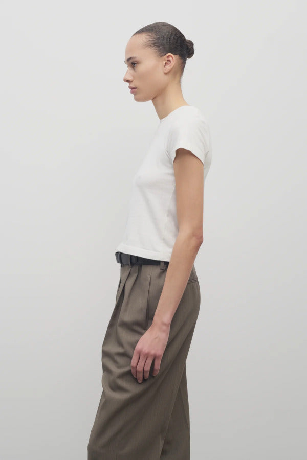 Side view of white tori top on model wearing khaki trousers and black belt, against white background.