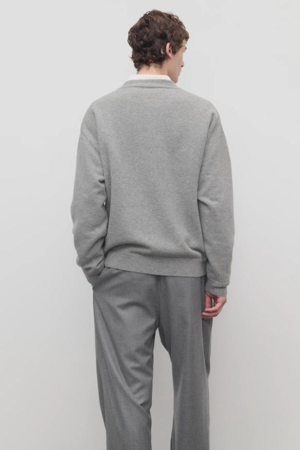 Back view of grey melange vonn cardigan on model wearing grey trousers and a white shirt, against a white background.