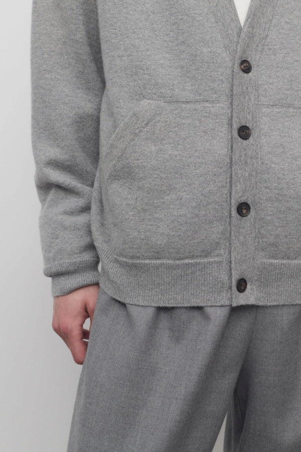 Front closeup view of grey melange vonn cardigan on model wearing white trousers and a white shirt, against a white background.