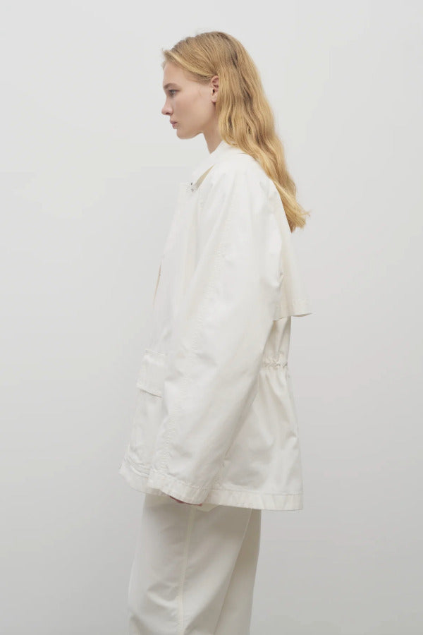 Side view of white elodianna jacket on model wearing white trousers and white shirt against a white background.