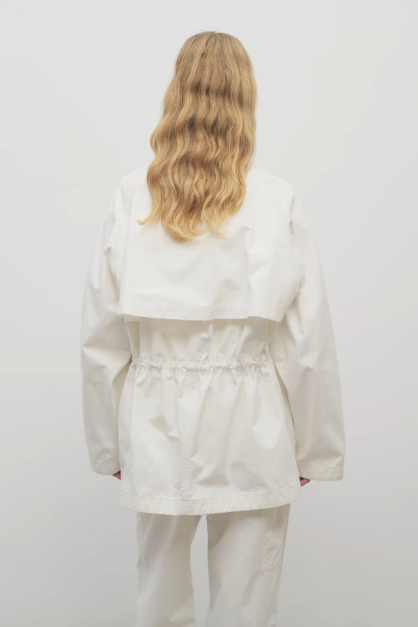 Back view of white elodianna jacket on model wearing white shirt and white trousers, against a white background.