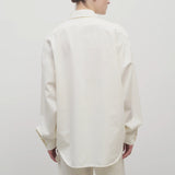 Back view of white erika shirt on model wearing white trousers, against white background.