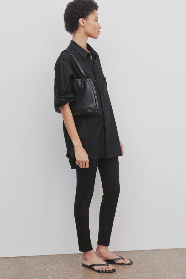 Side view of black woolworth on model wearing black tunic and black sandals, against a white background.