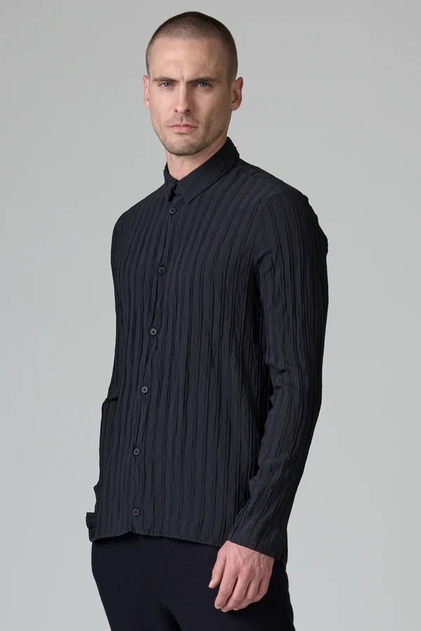 Side slanted view of blue loose fit striped shirt on model wearing black pants, against a grey background.