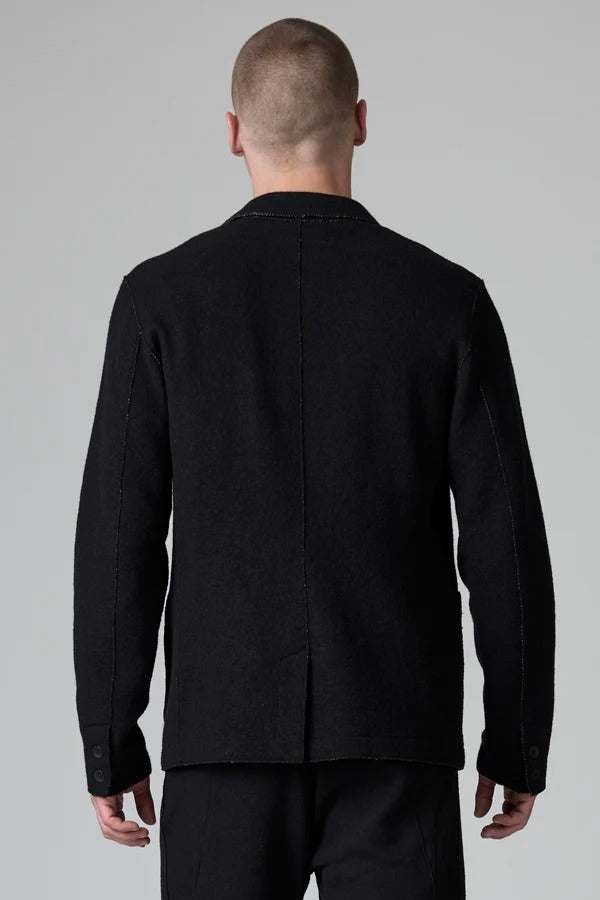 Back view of black/brown regular fit jacket on model wearing black pants, against a grey background.