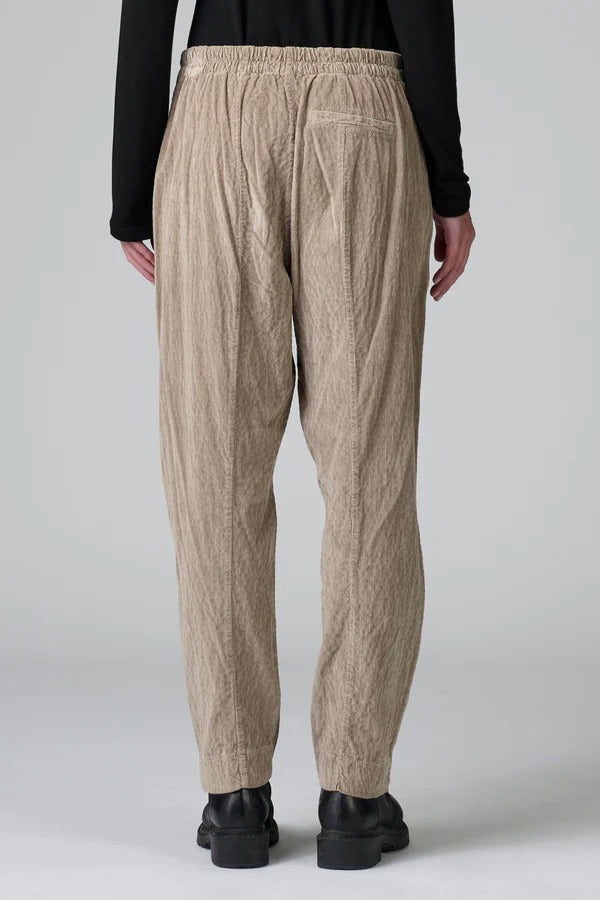 Back view of Camel Regular fit trousers on model wearing black top and boots, against a grey background.