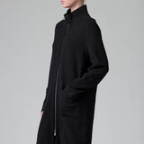Side view of black/anthracite straight coat on model wearing black pants, against a grey background.