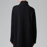 Back view of black/anthracite straight coat on model wearing black pants, against a grey background.