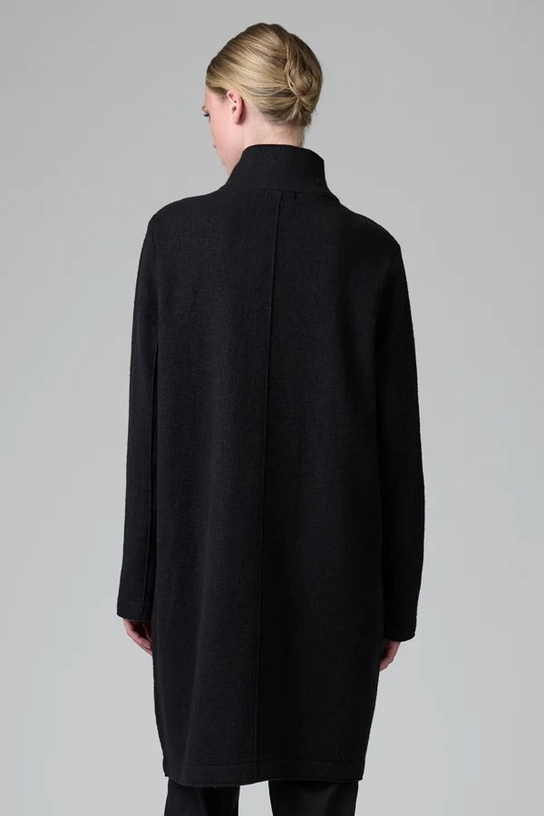 Back view of black/anthracite straight coat on model wearing black pants, against a grey background.