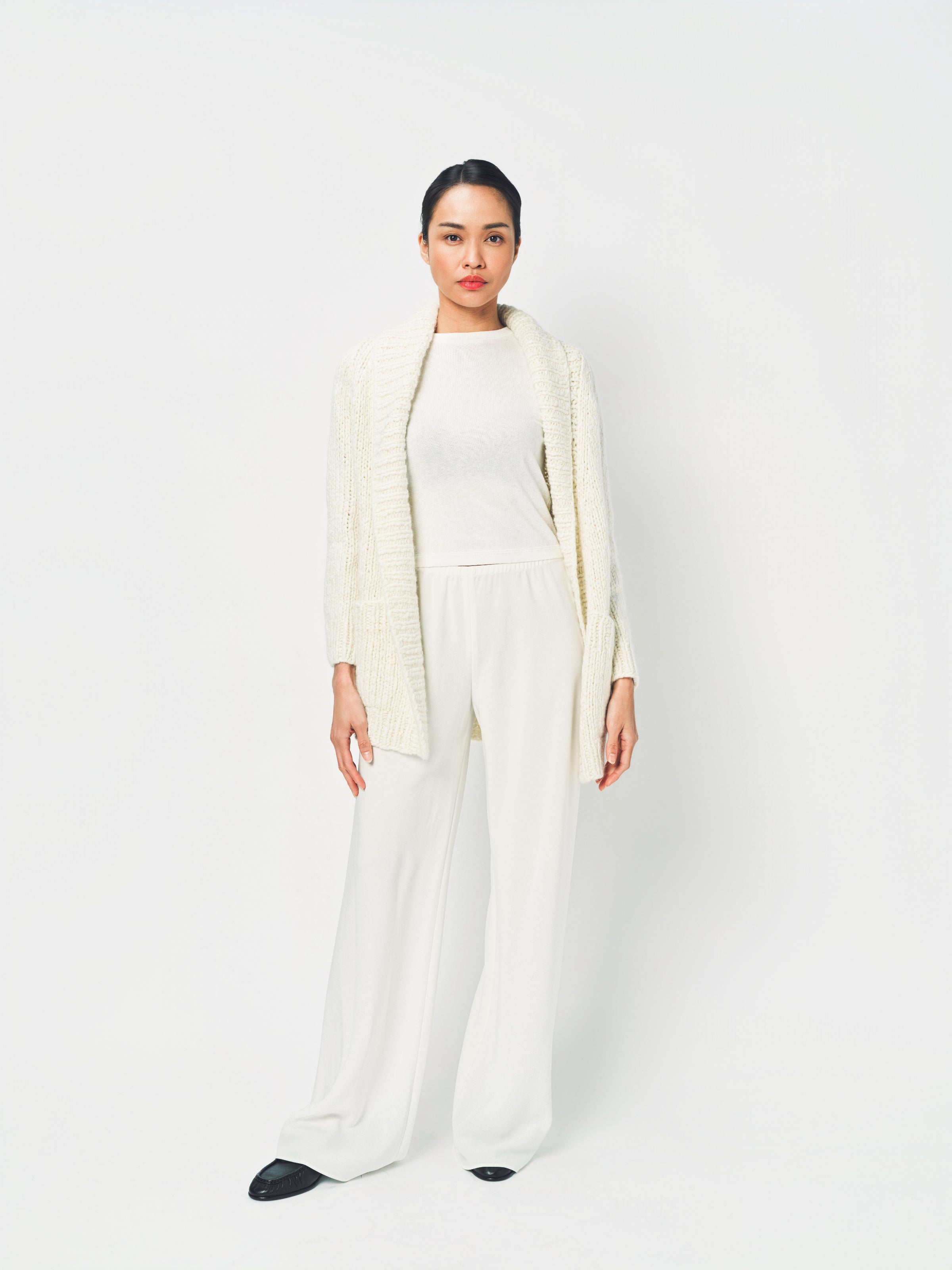 Woman wearing a long cream cardigan over a white outfit on a white background