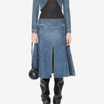 Front view of denim cropped jacket on model wearing black bodysuit, denim skirt and boots, against a white background.