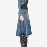 Side view of denim cropped jacket on model wearing black bodysuit, denim skirt and boots, against a white background.
