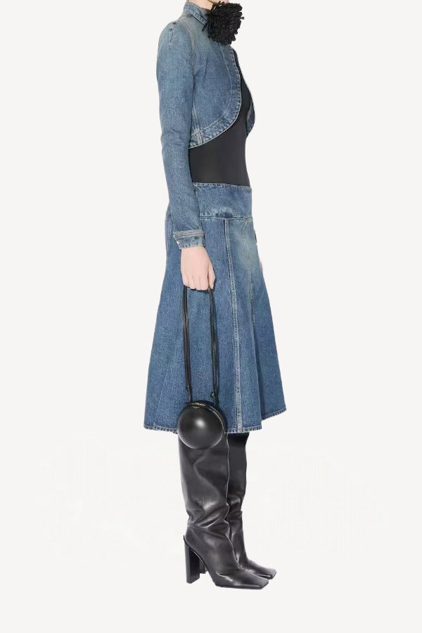 Side view of denim cropped jacket on model wearing black bodysuit, denim skirt and boots, against a white background.