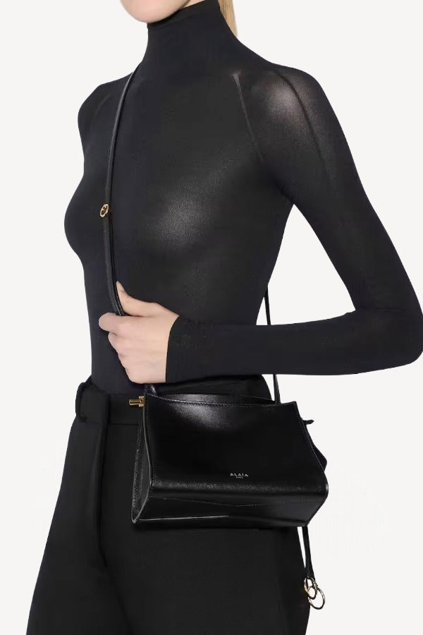 Front view of noir le click small square bag on model wearing black top and pants, against a white background.